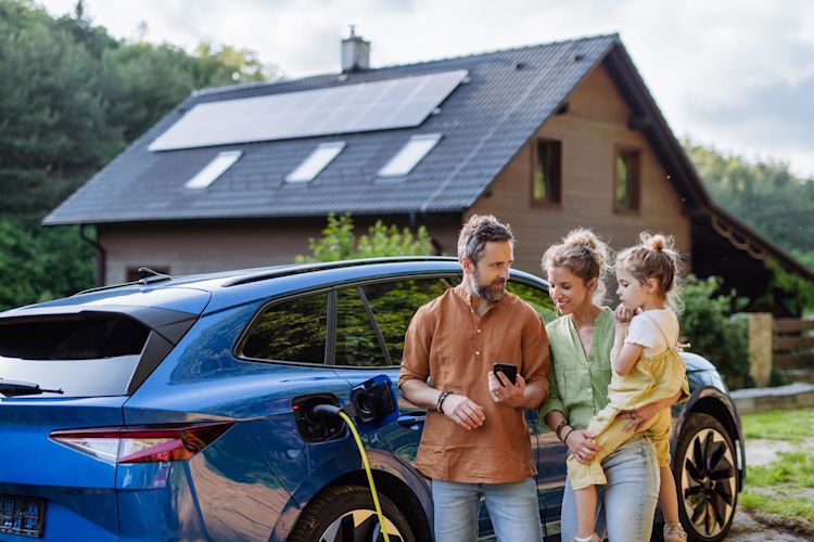 Ob Volleinspeisung oder Eigenbedarf - mit Solar auf dem Dach hat man viele Vorteile und Möglichkeiten Familie mit Mädchen laden Elektroauto vor dem Haus mit Solaranlage auf dem Dach