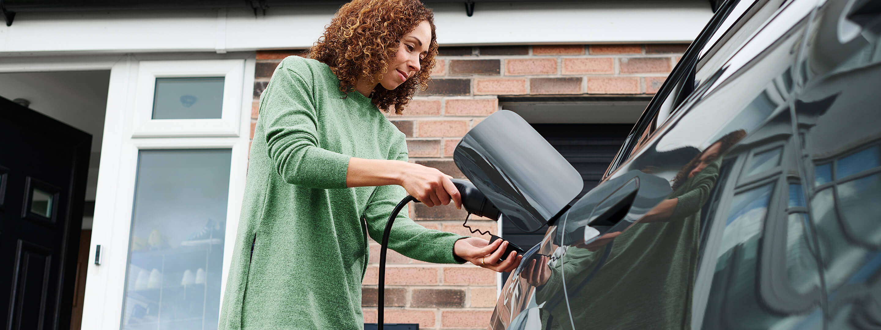 Frau hängt das Ladekabel für E-Auto über die Wallbox