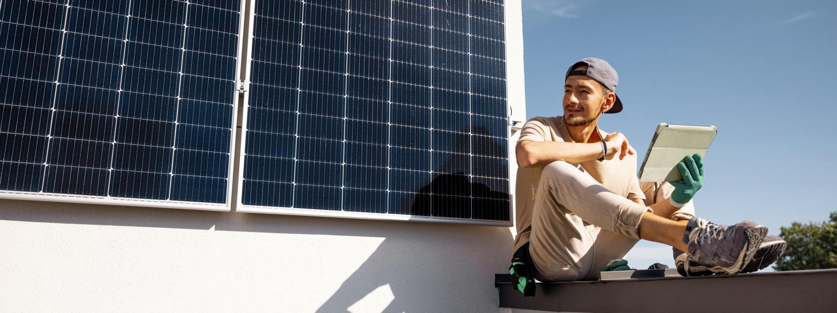 Mann prüft Solarmodule auf einem Dach mit Tablet