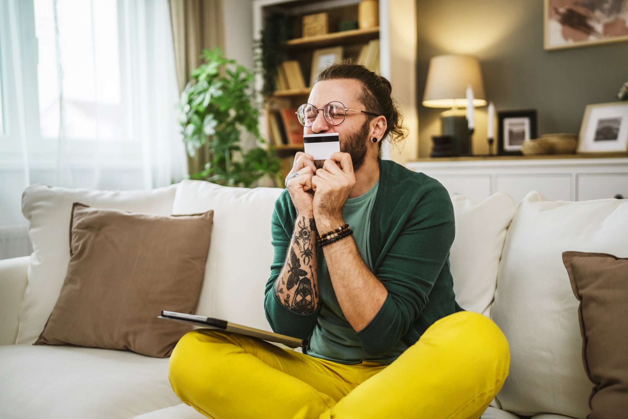 Foto von einem jungen Mann, der auf dem Sofa sitzt und seine Kreditkarte küsst